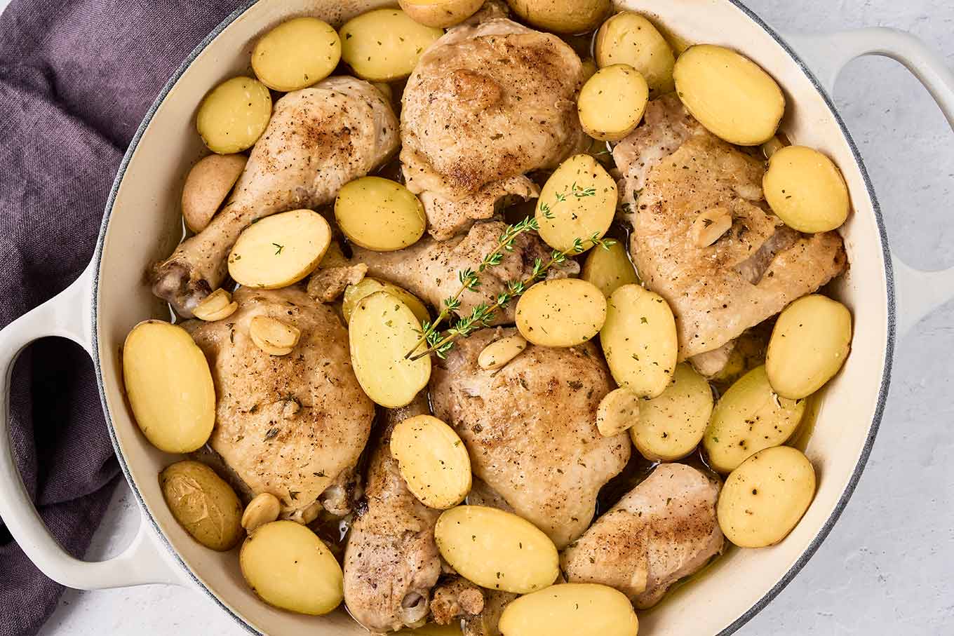 Browned chicken thighs and drumsticks topped with halved baby potatoes and garlic before braising.