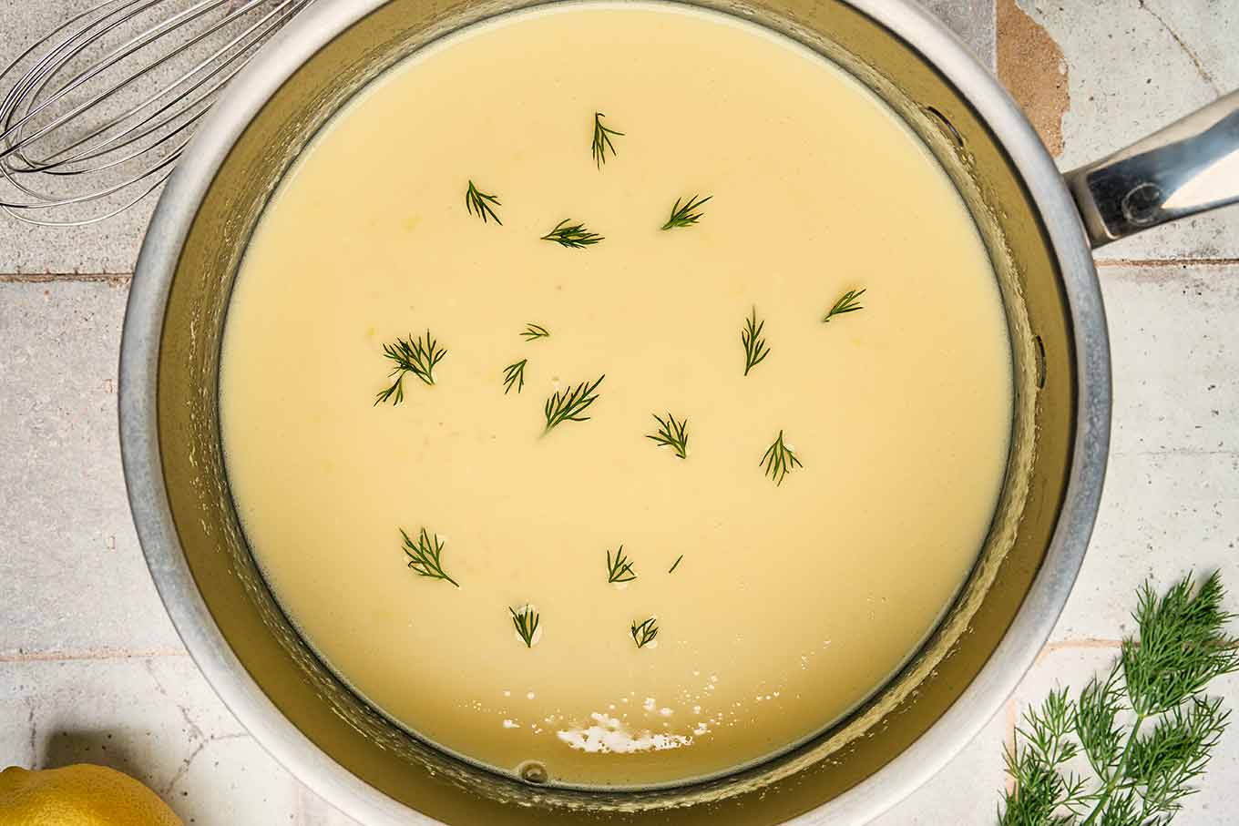Greek egg and lemon soup in a saucepan, gently thickened and garnished with fresh dill during preparation.
