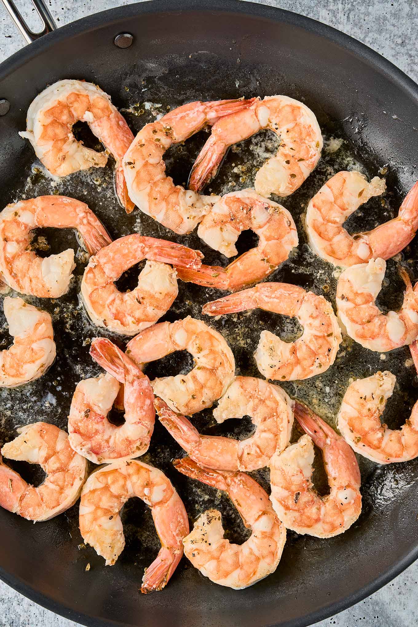 Shrimp saut&eacute;ing in a skillet, turning pink and opaque as they cook in olive oil.