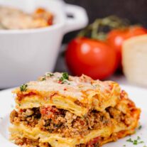 A slice of lasagna with layered no-boil noodles, four cheese filling, and Italian sausage in marinara, garnished with parsley on a white plate.