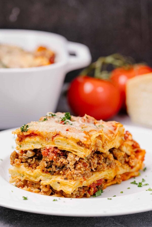 A slice of lasagna with layered no-boil noodles, four cheese filling, and Italian sausage in marinara, garnished with parsley on a white plate.