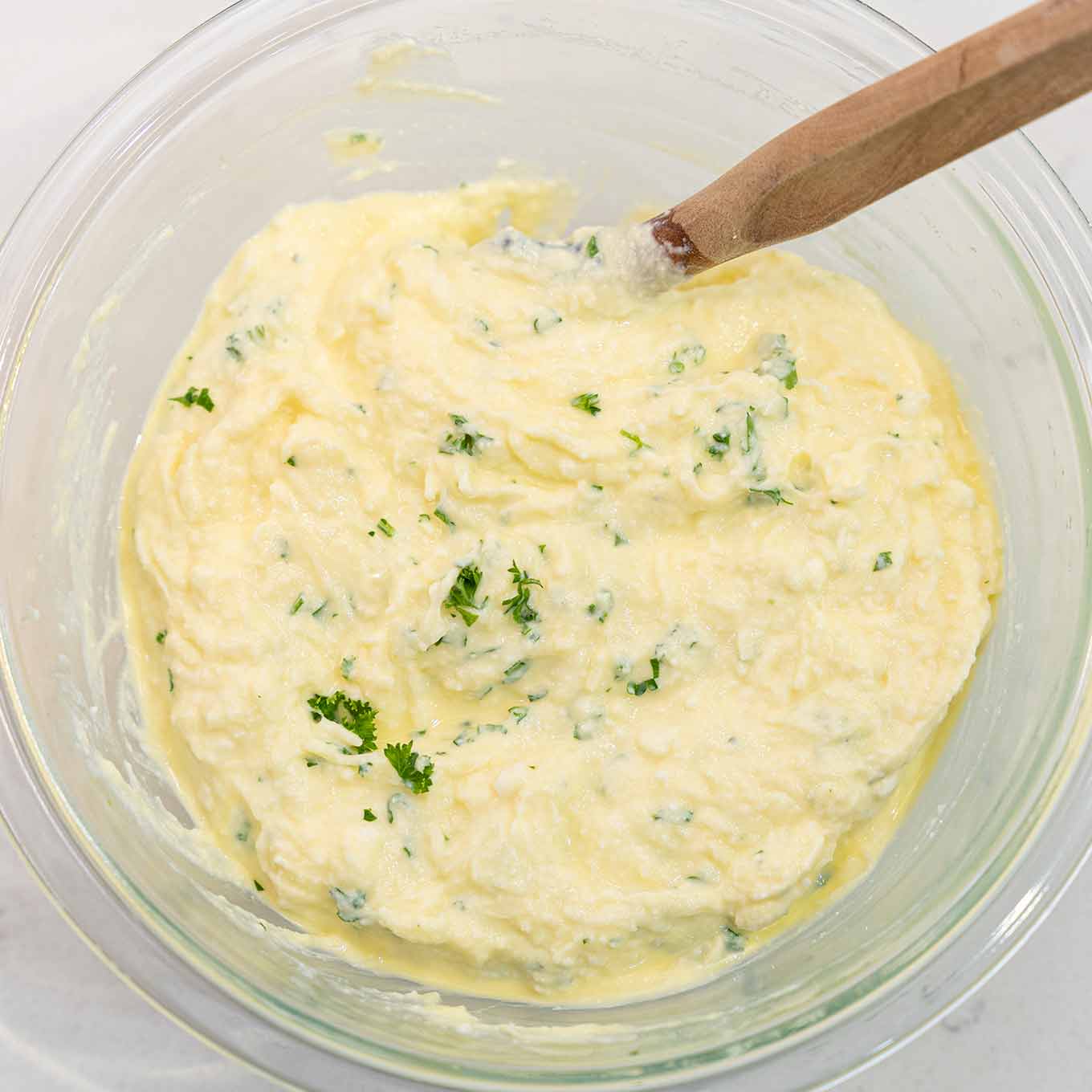 Ricotta cheese and egg mixture being combined with shredded mozzarella, Asiago, Parmesan, and parsley to make the cheese filling for sausage lasagna.