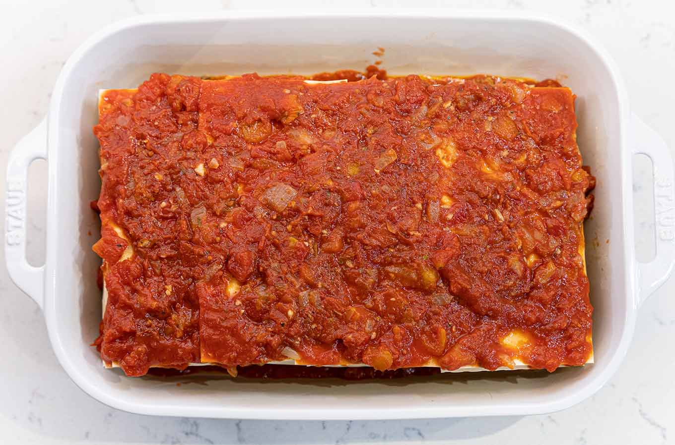 Fully assembled four cheese lasagna, topped with homemade marinara and ready to be covered and baked.