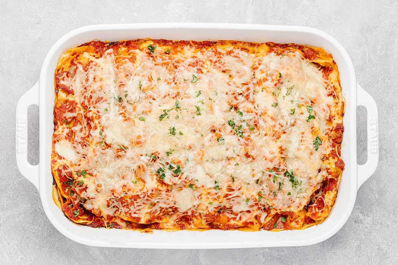 A fully-baked lasagna in its pan, melted cheese and a sprinkling of parsley on top, ready to be cut and served.