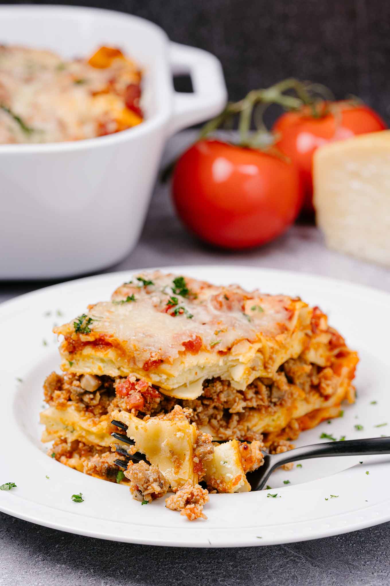 A single serving of four-cheese lasagna on a white plate with a forkful removed and ready to eat.