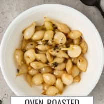 Roasted pearl onions with butter and thyme, lightly caramelized and arranged in a white serving bowl.