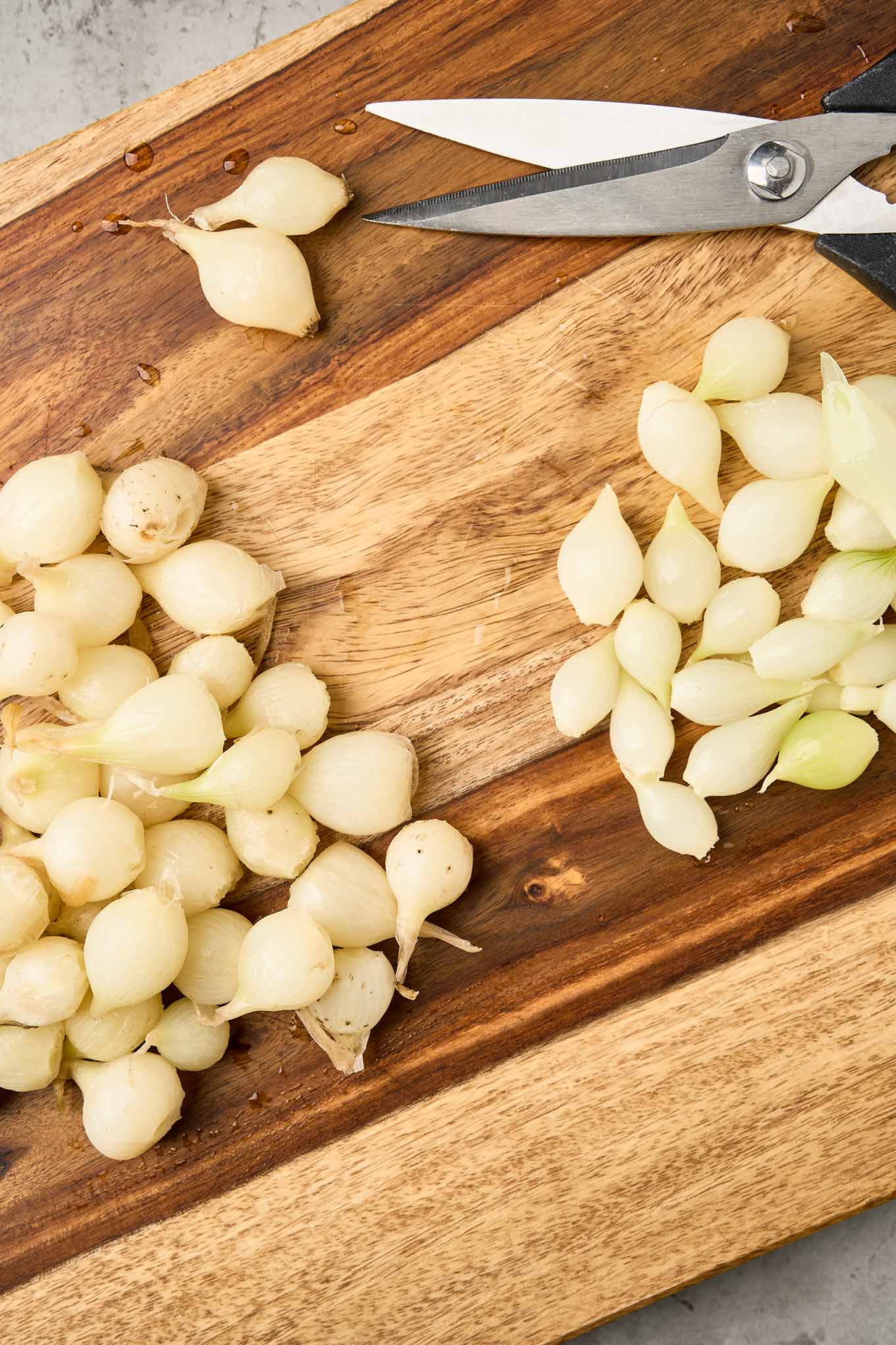 Trimming the root end of pearl onions with kitchen shears to remove the skins.