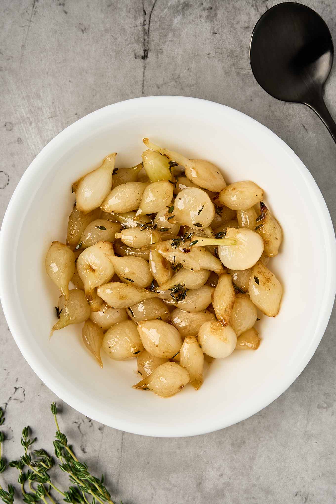 Roasted pearl onions with butter and thyme, lightly caramelized and arranged in a white serving bowl.