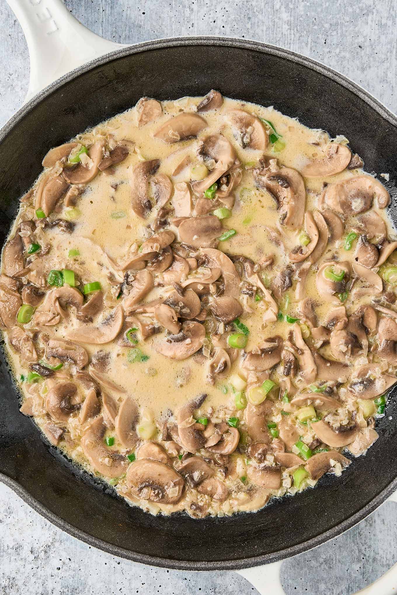 Cream added to saut&eacute;ed mushrooms with chopped scallions in a skillet for truffle mushroom pasta.