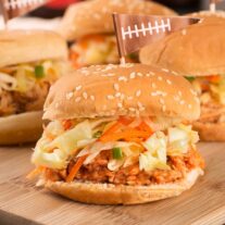 Instant Pot pulled chicken on slider rolls with coleslaw, arranged on a cutting board for serving.