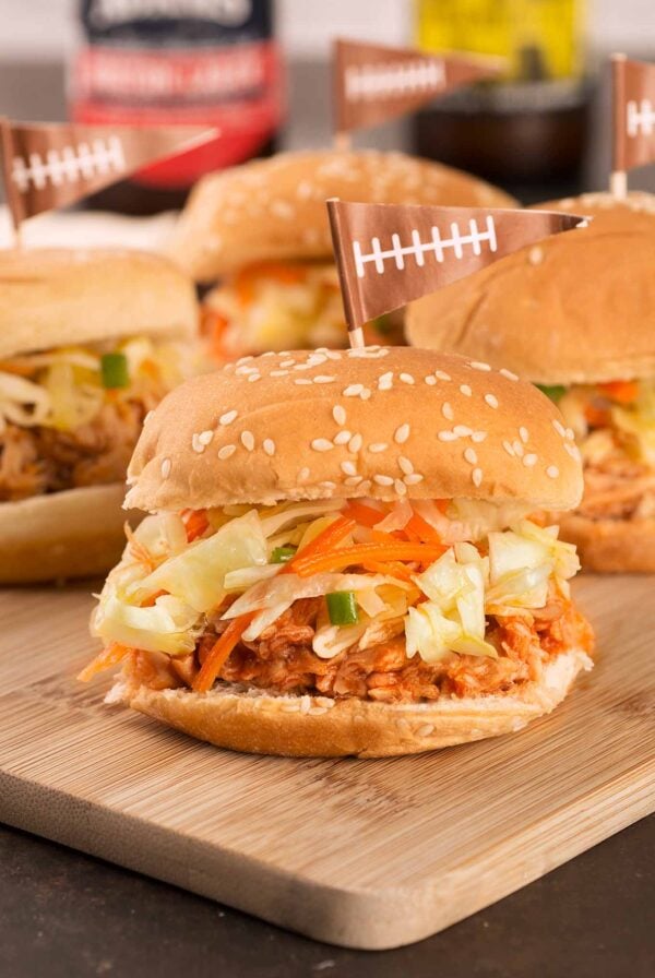 Instant Pot pulled chicken on slider rolls with coleslaw, arranged on a cutting board for serving.