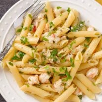 Lobster tail pasta with penne tossed in shallot butter and white wine sauce on a white plate with parsley garnish.