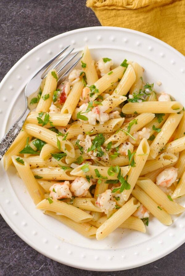 Lobster tail pasta with penne tossed in shallot butter and white wine sauce on a white plate with parsley garnish.