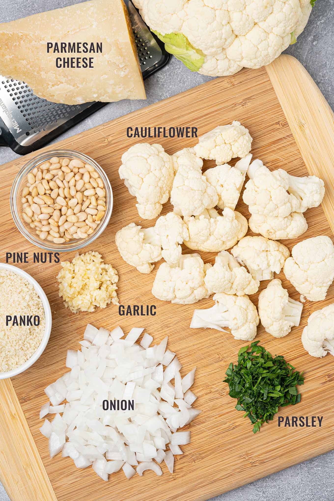 Ingredients for roasted cauliflower pasta arranged on a cutting board, including cauliflower florets, Parmesan, pine nuts, panko, onion, garlic, and parsley.