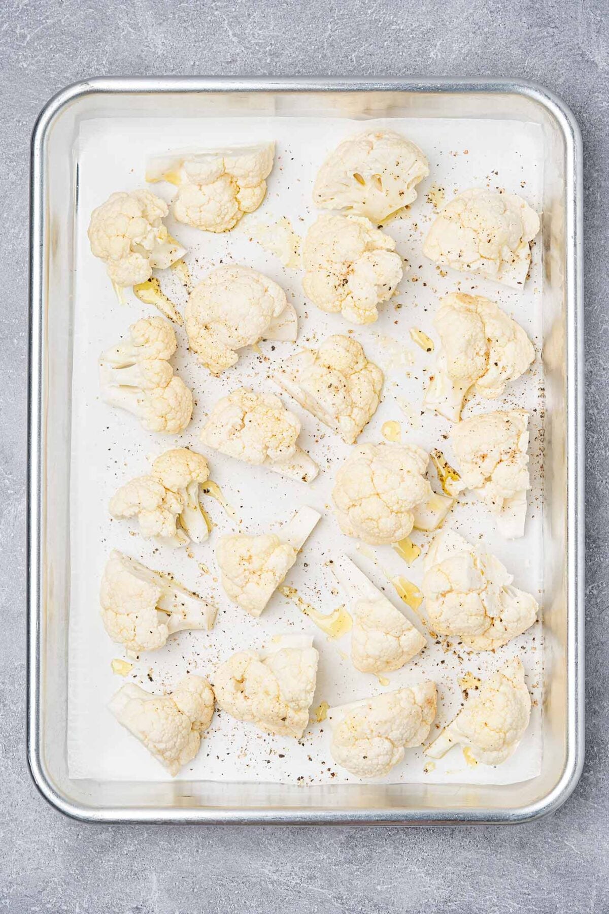 Cauliflower florets arranged on a parchment-lined baking sheet, drizzled with olive oil and seasoned with salt and pepper.