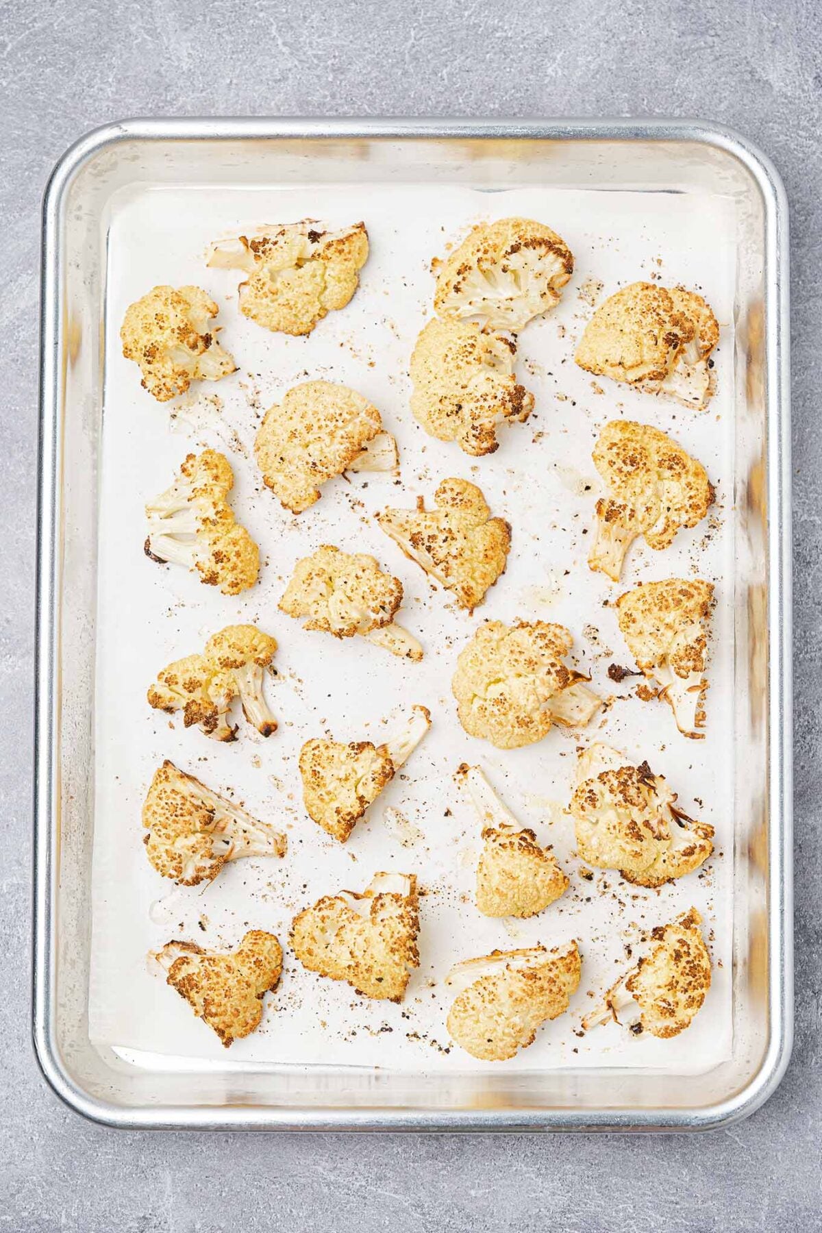 Roasted cauliflower florets on a parchment-lined baking sheet, lightly caramelized and golden brown.