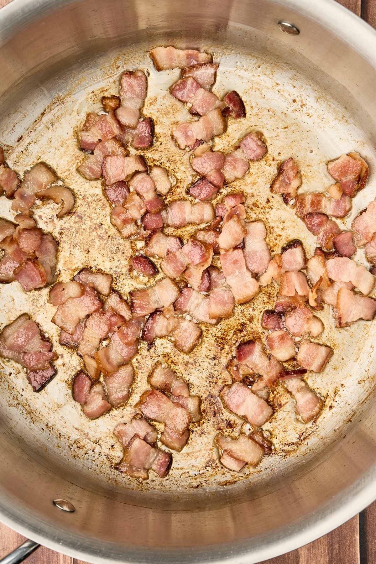 Thick-cut bacon pieces browning in a stainless steel pot for fire-roasted tomato and bacon soup.