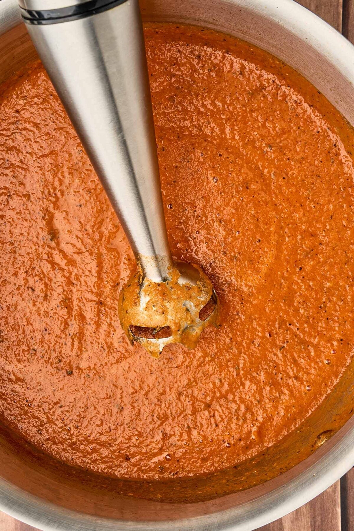 Immersion blender pur&eacute;eing fire-roasted tomato and bacon soup until smooth in a stainless steel pot.