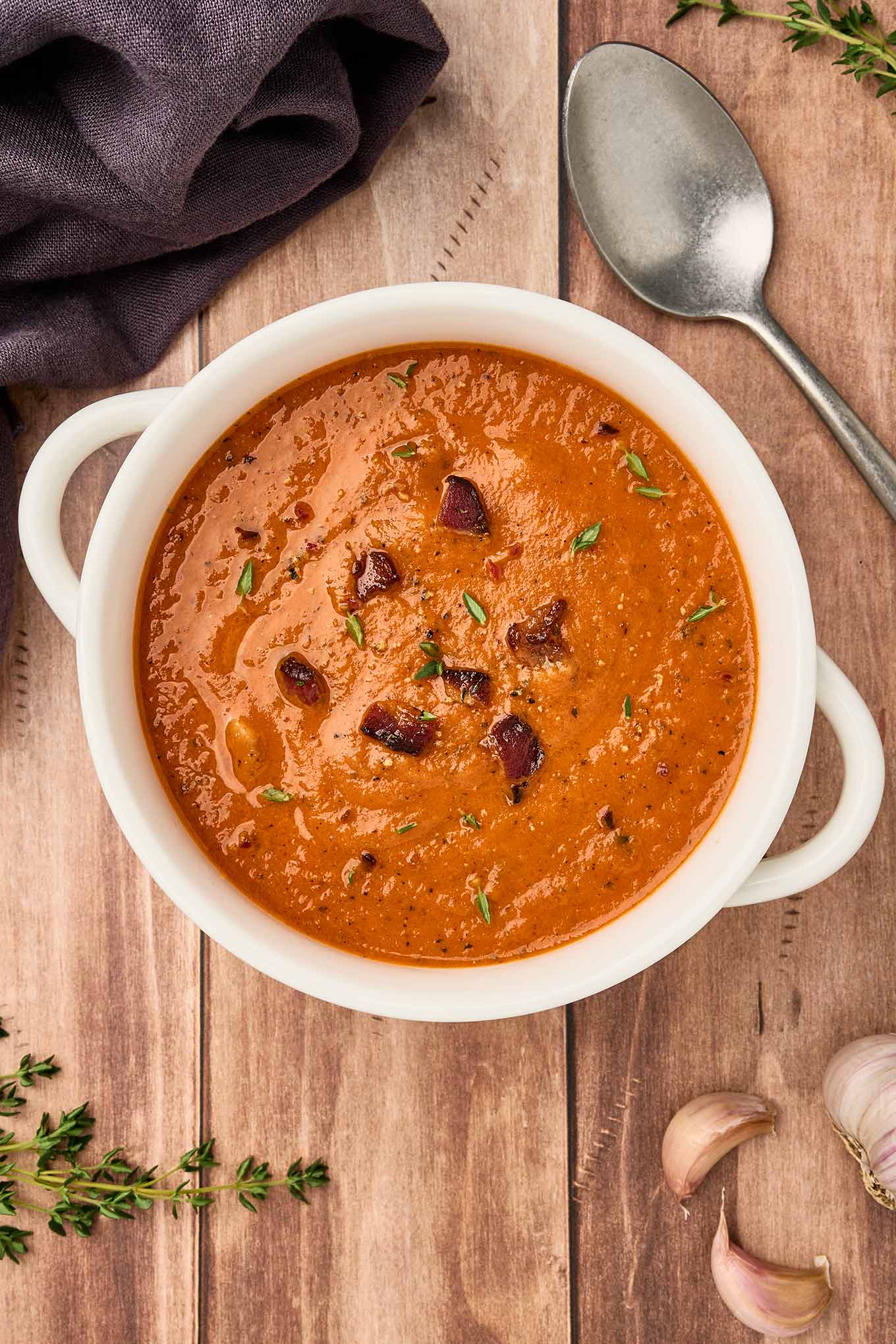 A serving of fire-roasted tomato and bacon soup in a white bowl, garnished with bacon pieces and fresh thyme.