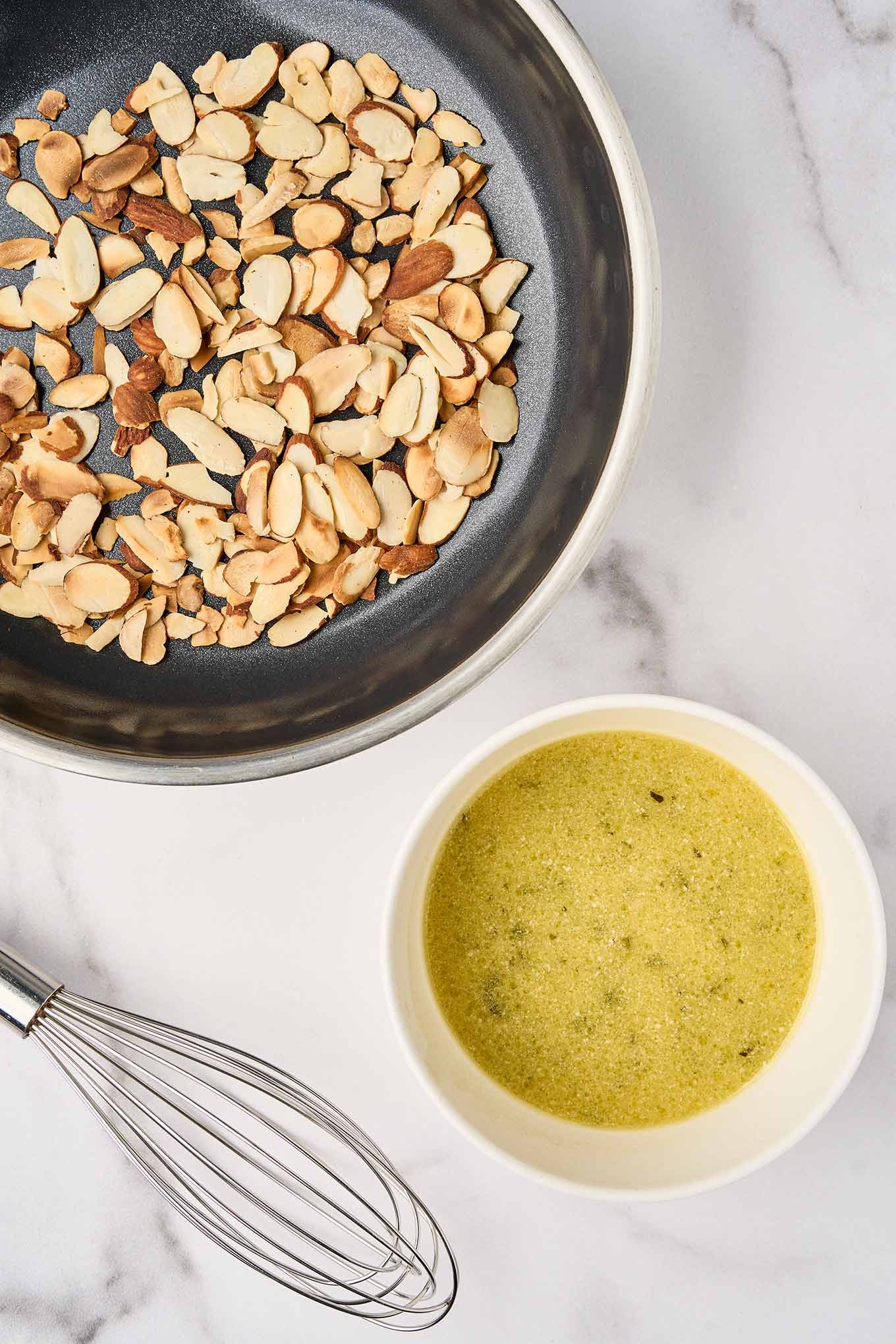Sliced almonds toasting in a pan with whisked balsamic dressing for spinach and strawberry salad.