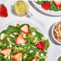 Spinach and strawberry salad with balsamic dressing served with goat cheese and sliced almonds on white plates.