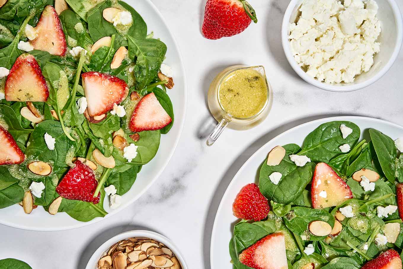 Plated spinach and strawberry salad with creamy basil balsamic dressing, goat cheese crumbles, and toasted almonds.