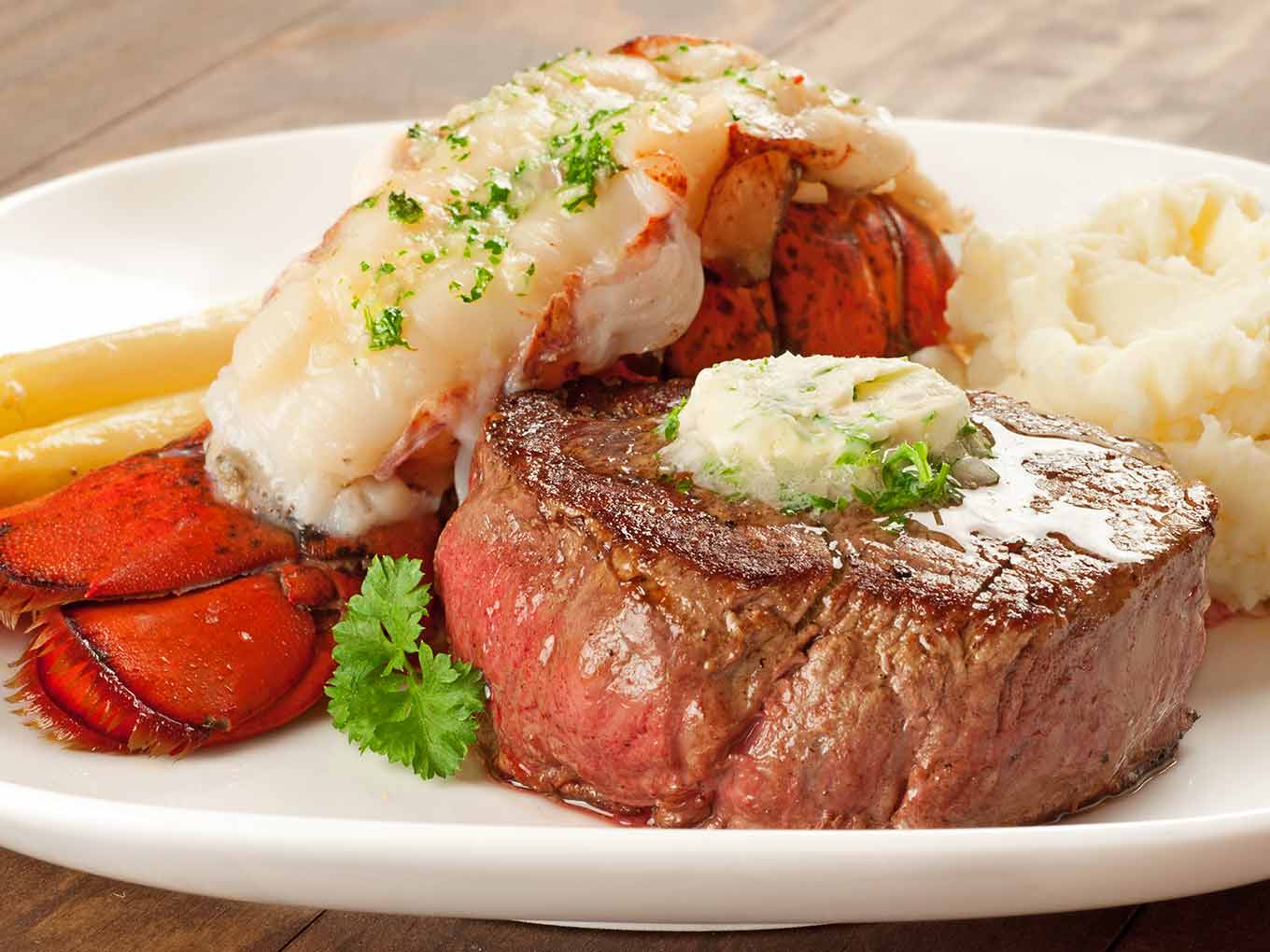 Filet mignon and lobster tail plated together with melted compound butter and parsley garnish.
