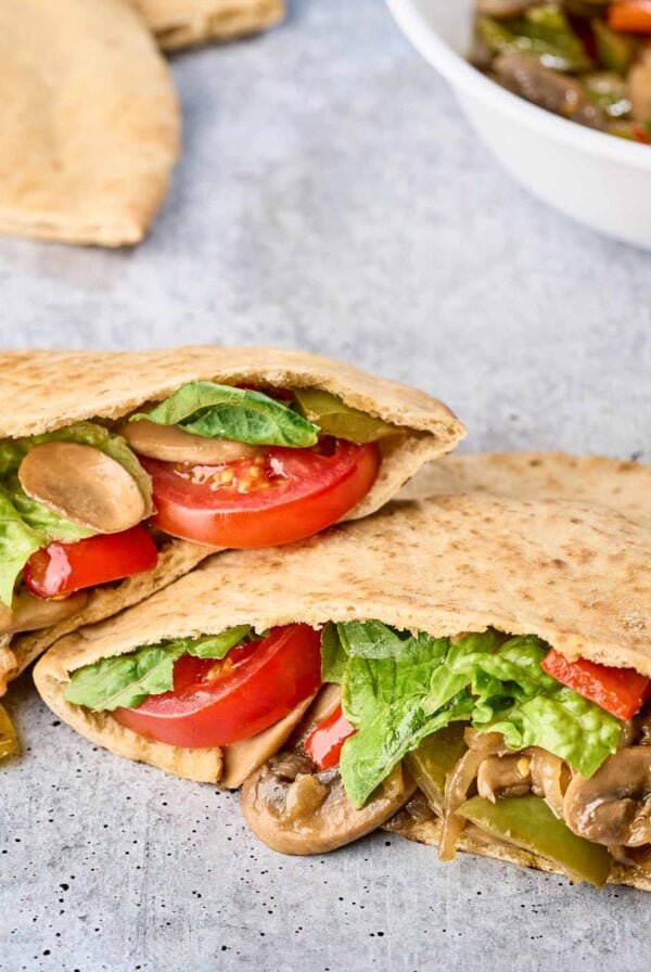 Vegetable pita melt with saut&eacute;ed mushrooms, peppers, melted cheese, lettuce, and tomato - extra filling and pitas in the background.