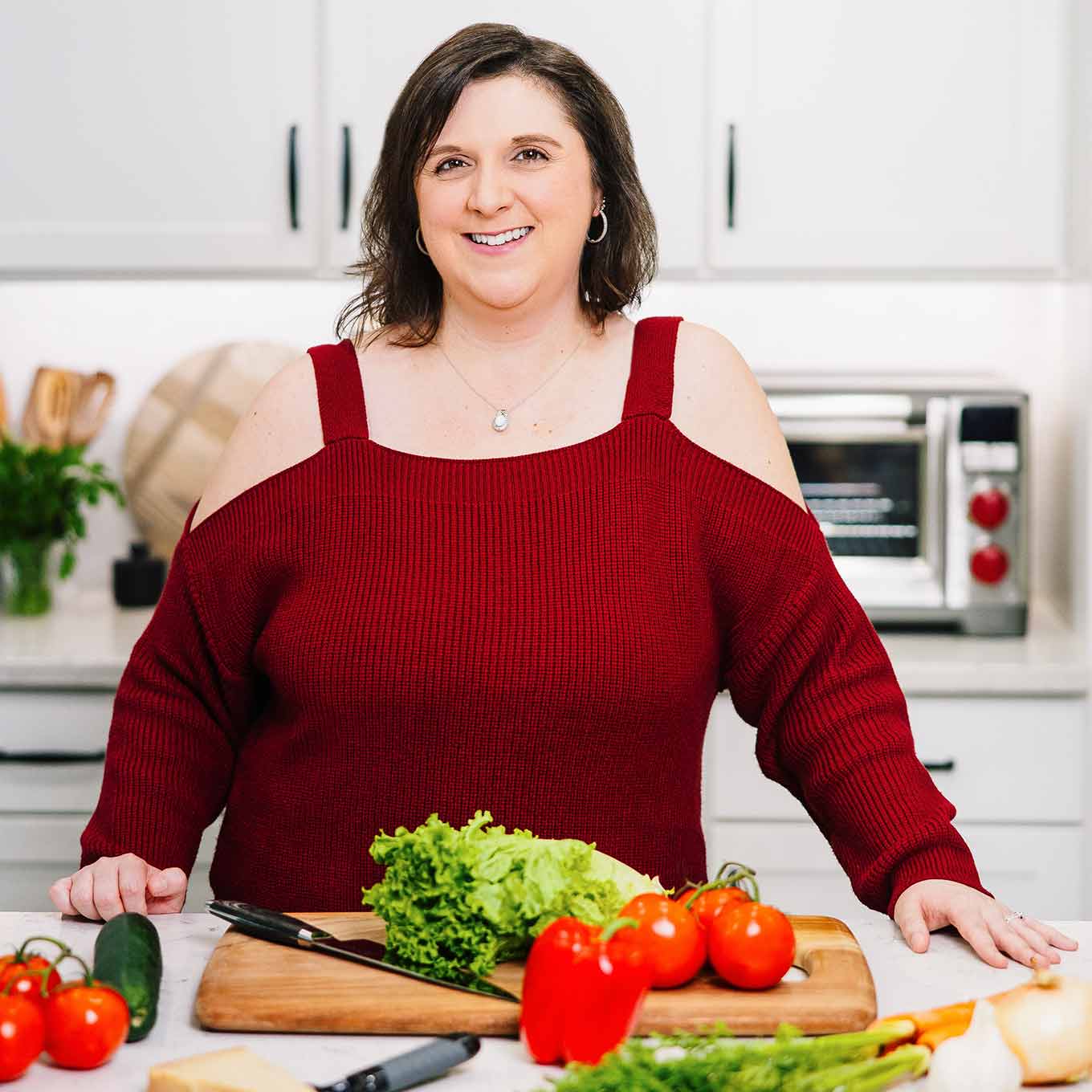 Erika Pitera, recipe creator and food stylist at MyGourmetConnection, standing in a kitchen beside a cutting board with fresh salad ingredients.