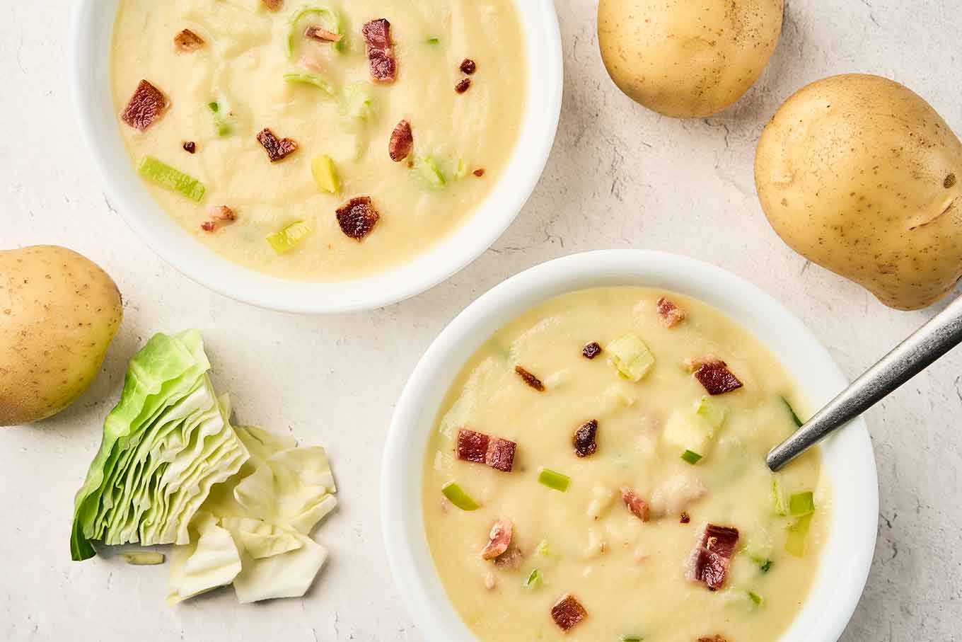 Creamy cabbage leek potato soup topped with bacon and sautéed leeks in white bowls.