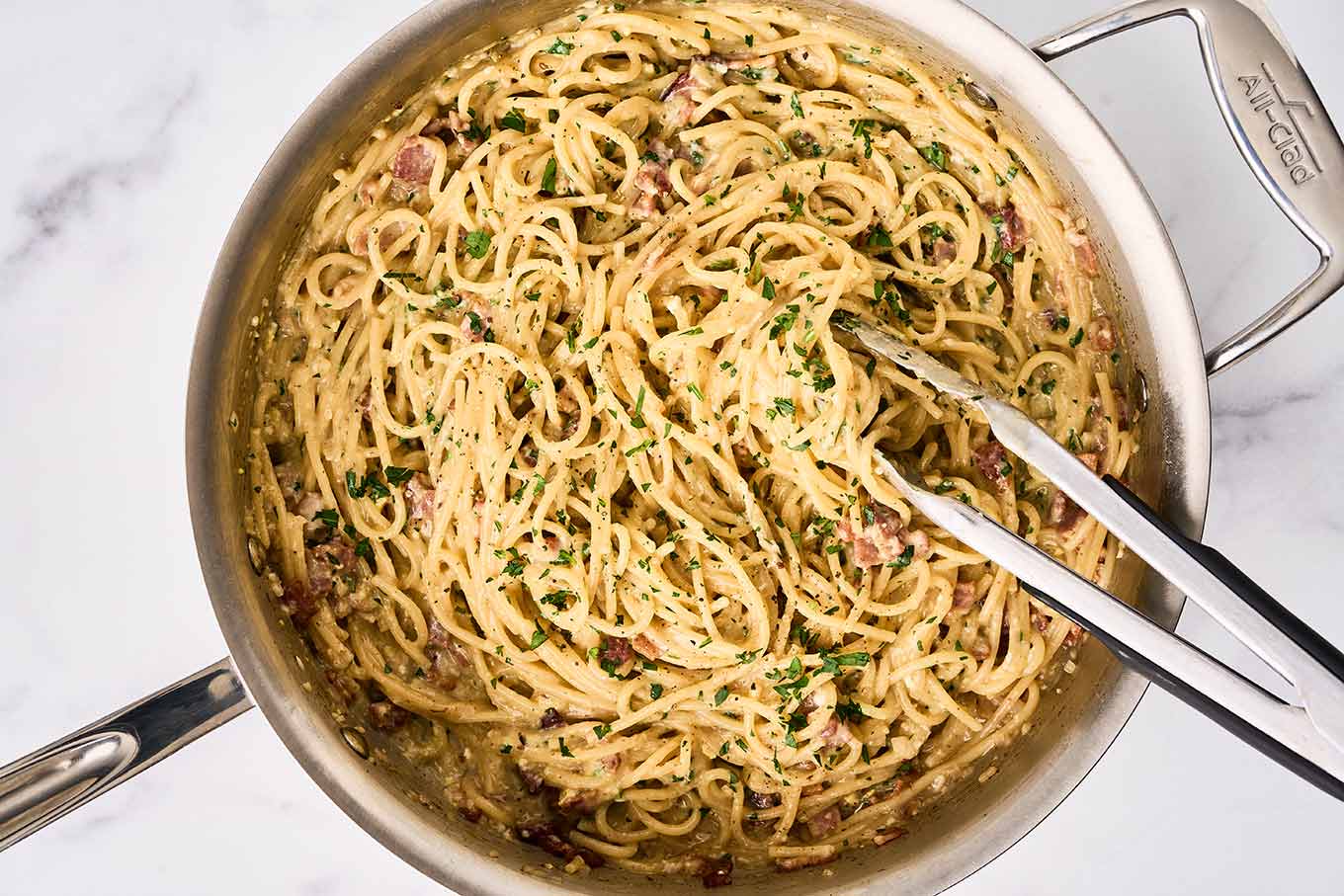 One-pot spaghetti carbonara being tossed with egg and Parmesan mixture with bacon in a stainless skillet.
