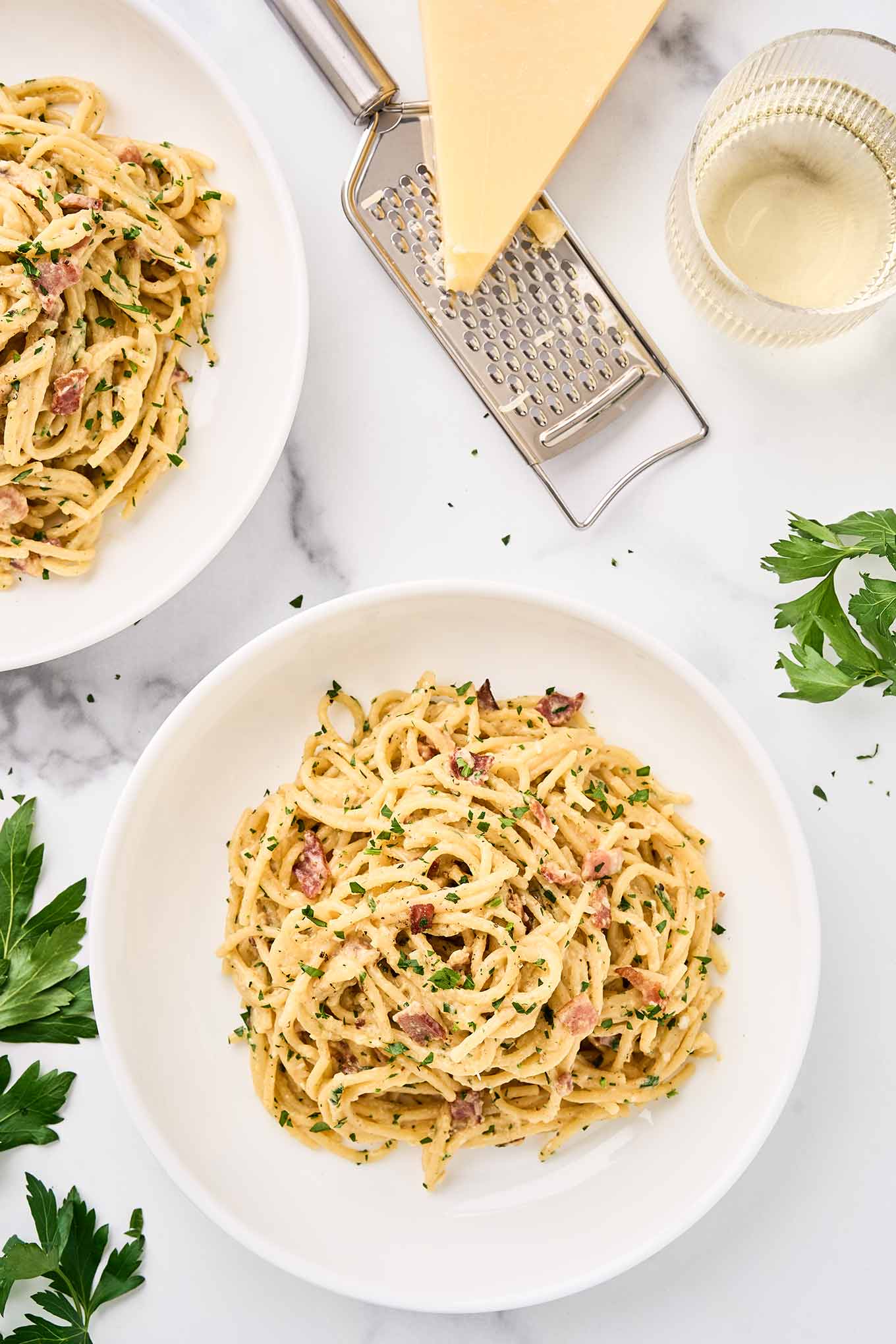 One-pot spaghetti carbonara plated with bacon, Parmesan, and parsley, served with grated cheese and white wine on the side.