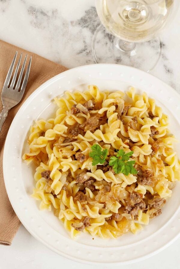 Pasta with caramelized onions and Italian sausage served on a white plate, garnished with parsley.
