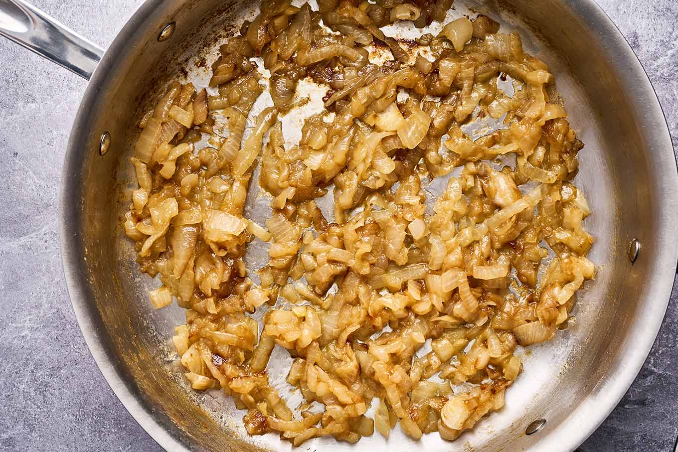 Caramelized onions cooking in a stainless pan for pasta with caramelized onions and sausage.
