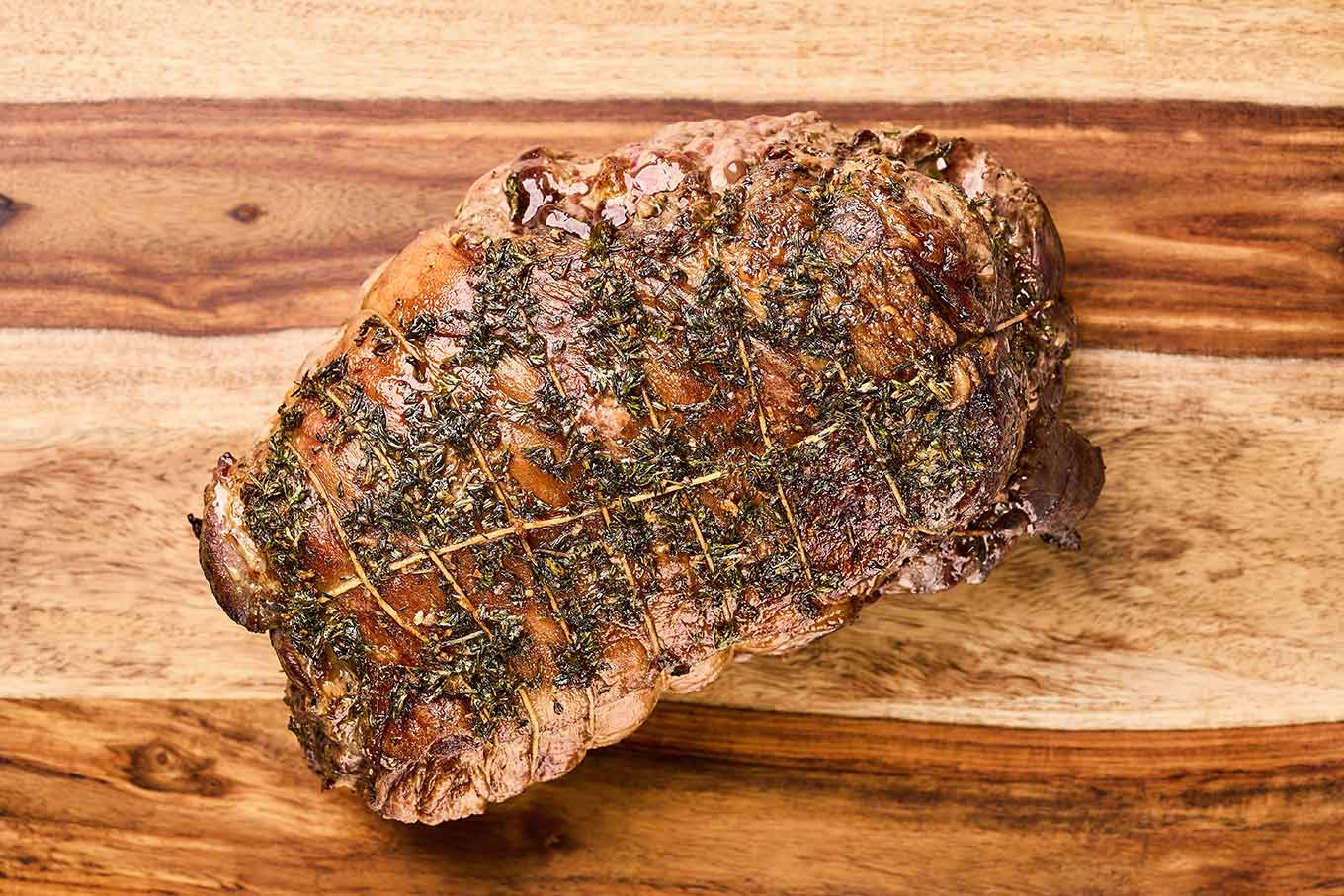 Herb roasted boneless leg of lamb resting on a cutting board before carving.