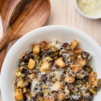 Warm Brussels sprouts Caesar salad with roasted sprouts, croutons, and grated Parmesan in a white serving bowl.