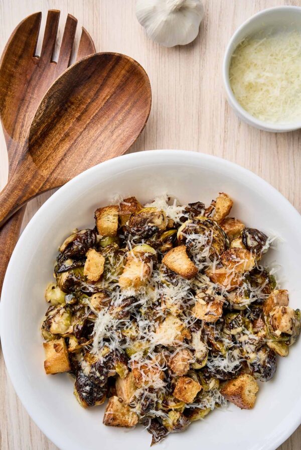 Warm Brussels sprouts Caesar salad with roasted sprouts, croutons, and grated Parmesan in a white serving bowl.