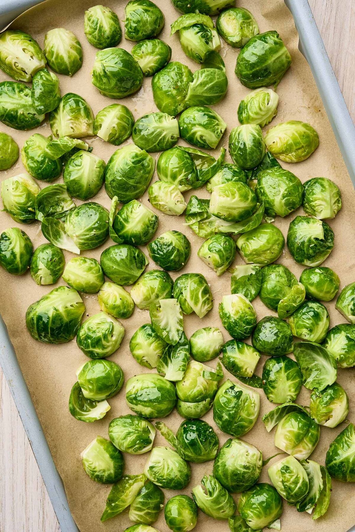 Halved Brussels sprouts tossed with olive oil on a baking sheet ready to roast.