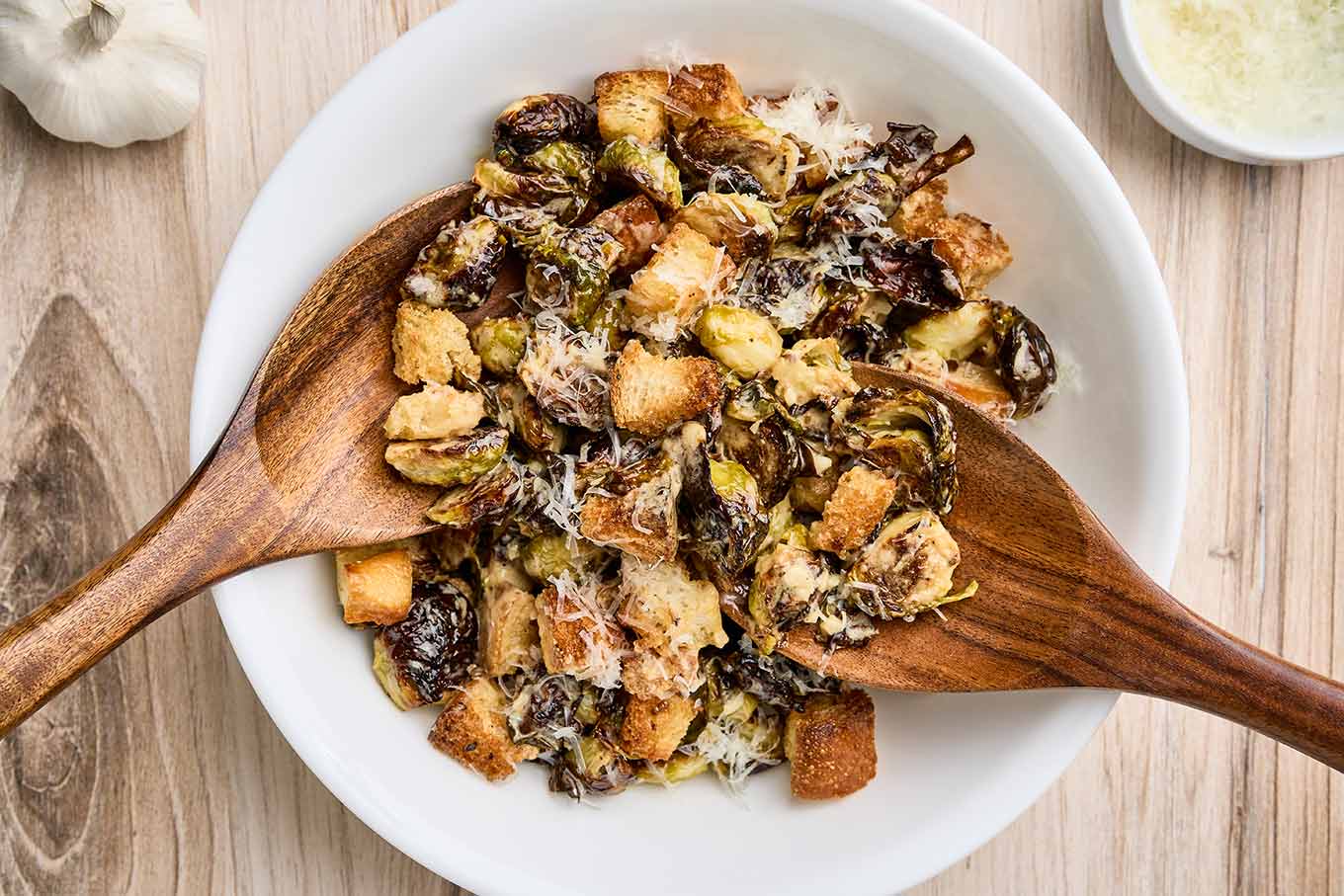 Warm Brussels sprouts Caesar salad being tossed with roasted sprouts, croutons, and grated Parmesan.