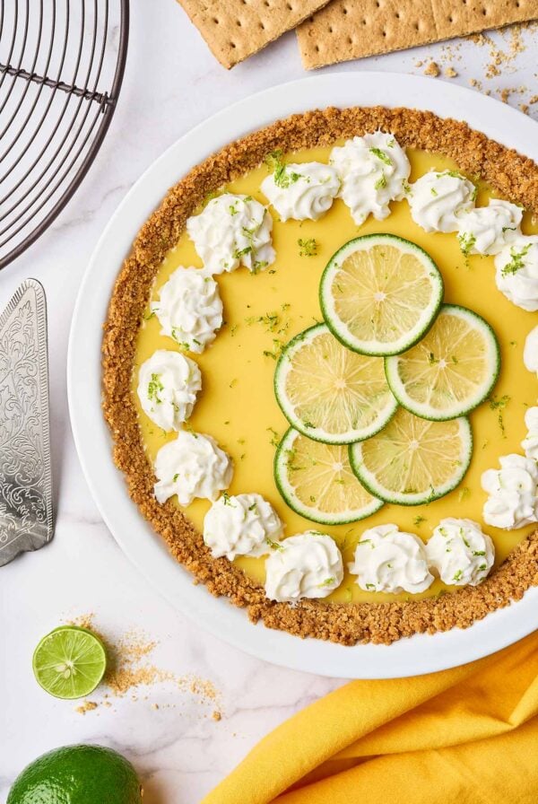 Florida Key lime pie with graham cracker crust, topped with whipped cream and lime slices in a white pie plate.