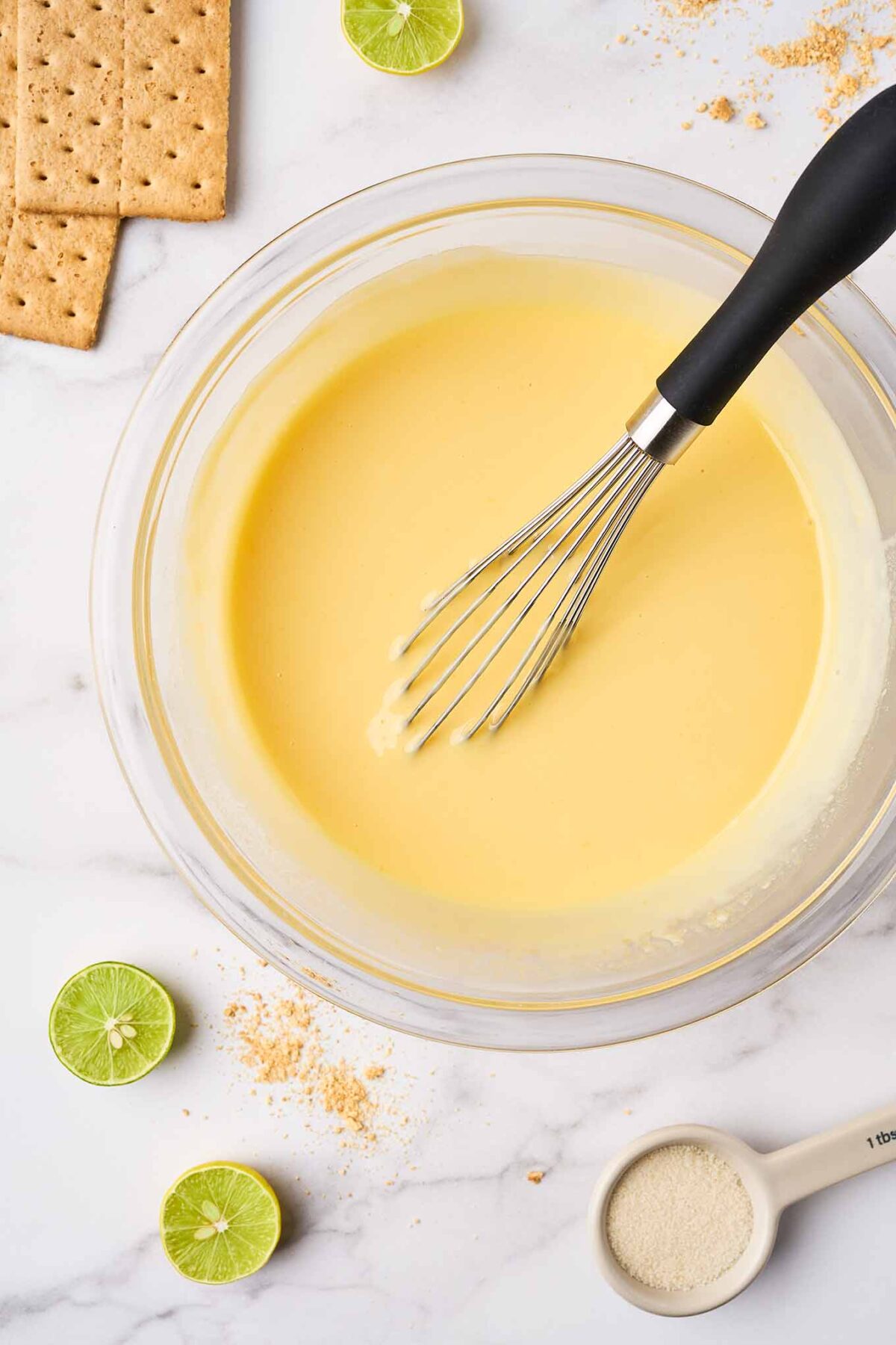 Key lime pie filling made with egg yolks, lime juice, and sweetened condensed milk being whisked in a bowl.