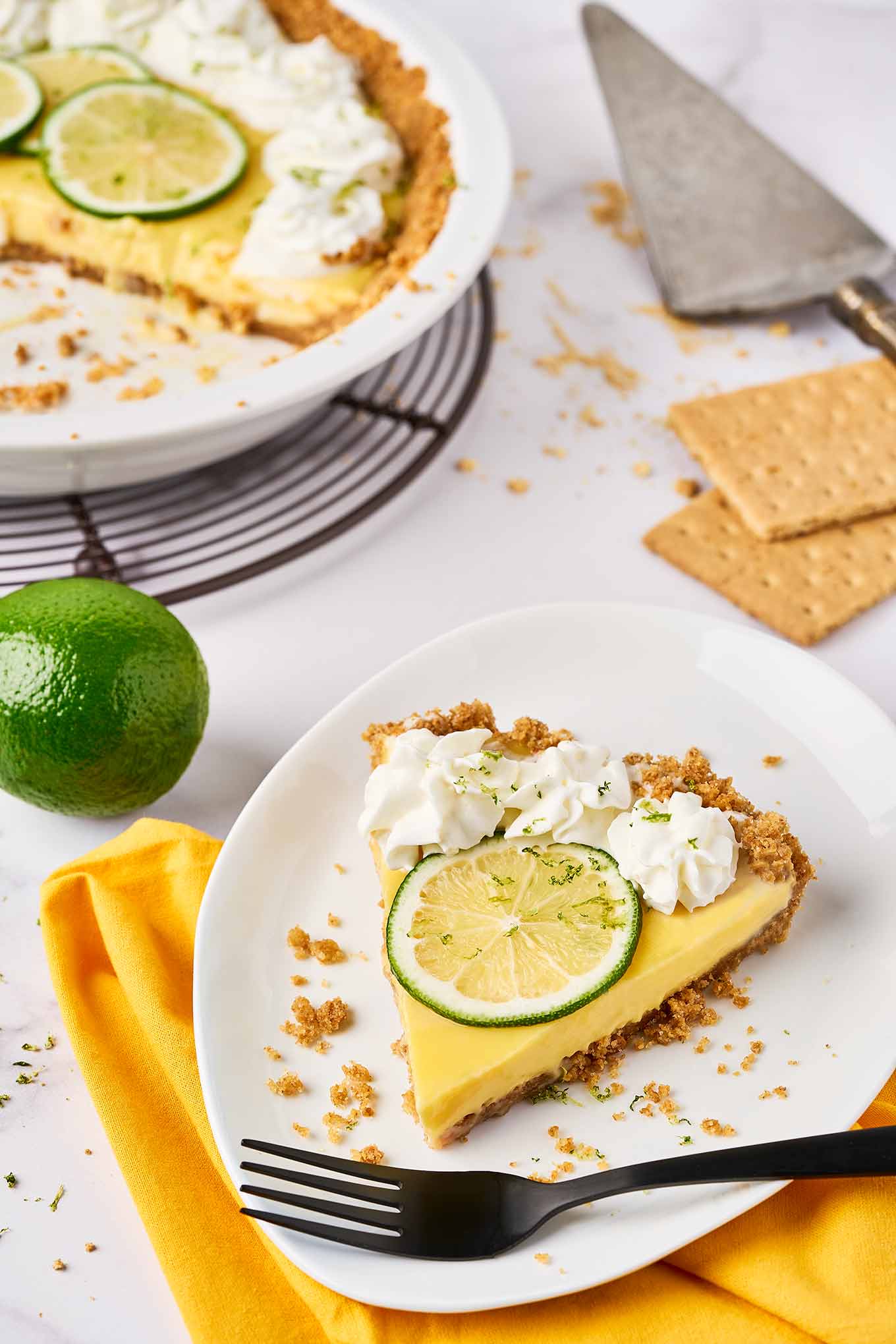 Slice of Florida Key lime pie with graham cracker crust, topped with whipped cream and lime slice on a white plate.