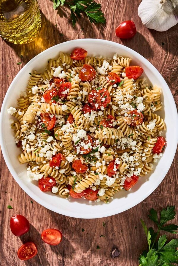 Goat cheese pasta with fresh tomatoes, rotini, toasted pine nuts, and parsley in a white serving bowl.