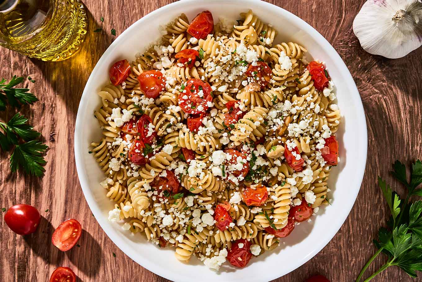 Goat cheese pasta with fresh tomatoes, rotini, toasted pine nuts, and parsley in a white pasta bowl.