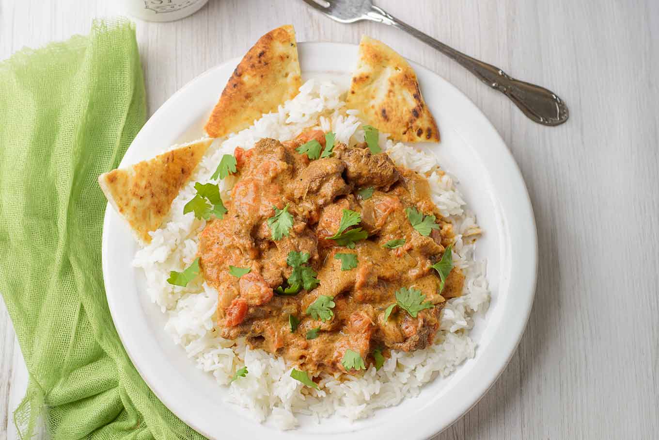 A serving of Instant Pot chicken tikka masala served over white rice, garnished with cilantro - toasted naan on the side.