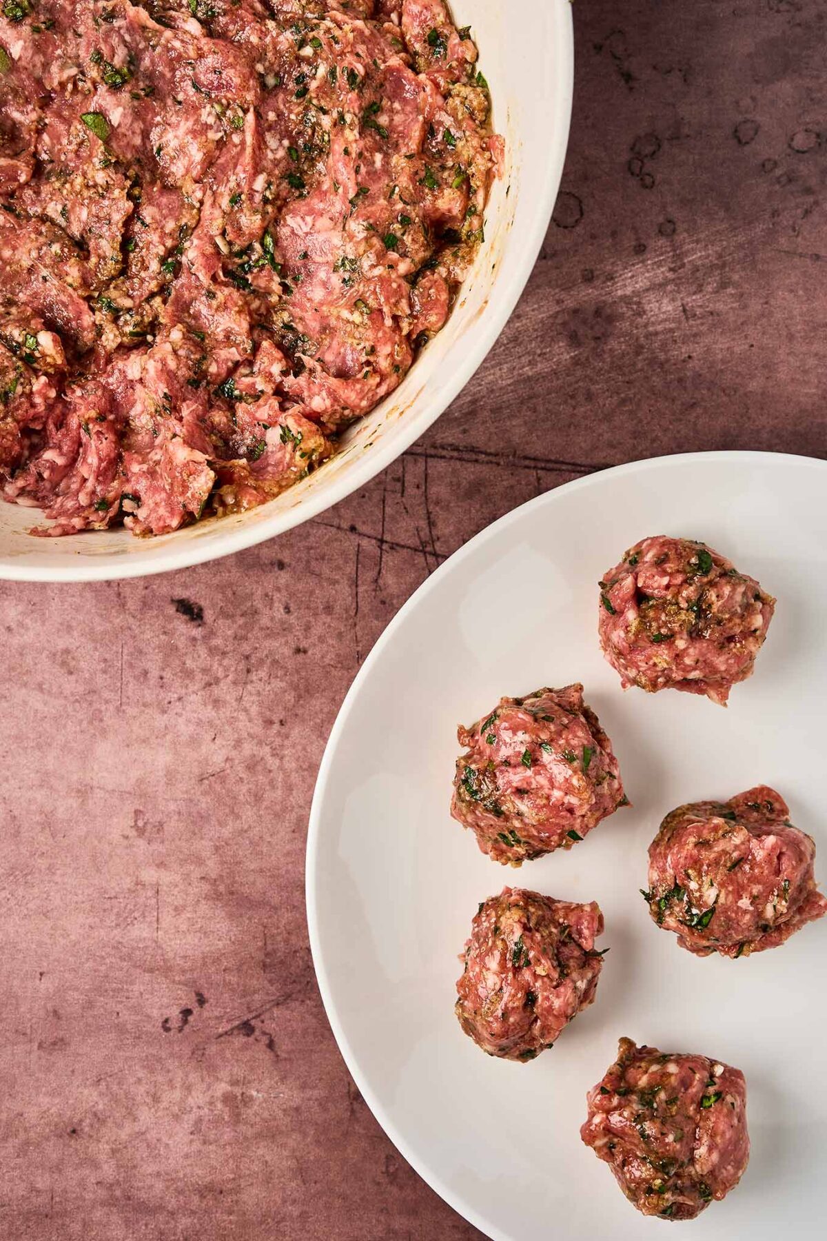 Moroccan meatball mixture in a bowl with raw meatballs being formed on a plate.