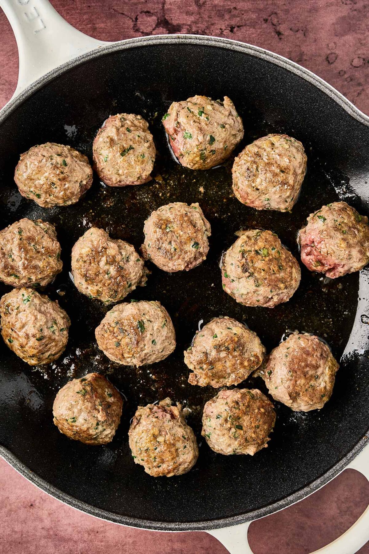 Moroccan meatballs browning in a skillet with lightly seared exterior and visible herbs.