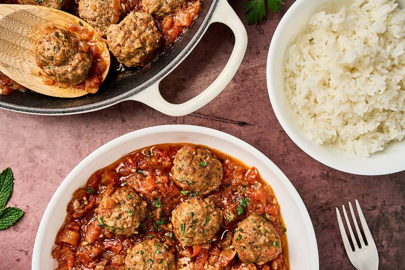 Moroccan meatballs in tomato sauce plated with white rice, with skillet of meatballs and bowl of rice in the background.