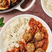 Moroccan meatballs in tomato sauce served with white rice on a plate, with skillet of meatballs and fresh mint on the side.