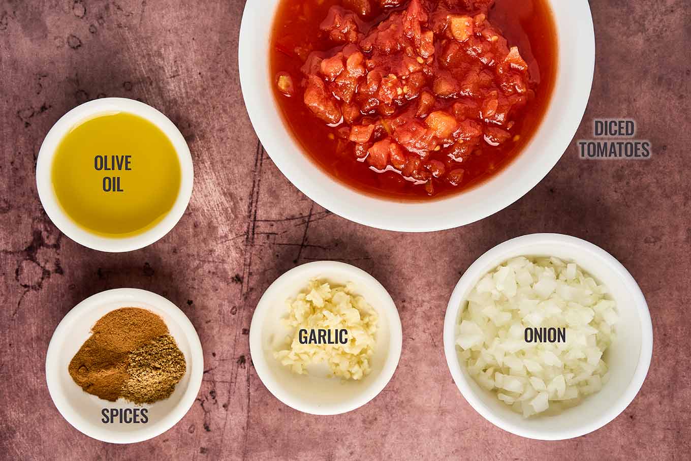 Ingredients for Moroccan meatballs in tomato sauce including diced tomatoes, onion, garlic, olive oil, and spices.